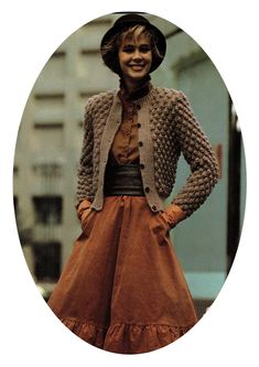 a woman wearing a brown dress and jacket with a hat on her head standing in front of a building