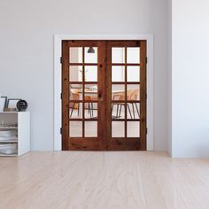 an empty room with two wooden doors leading to a dining table and chairs in the background