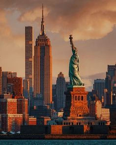 the statue of liberty in new york city is lit up at sunset with skyscrapers behind it