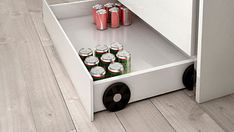 an open cabinet with many cans of soda in it on the floor next to a wooden floor