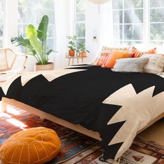 a bed with black and white comforter in a bedroom next to a plant on the floor