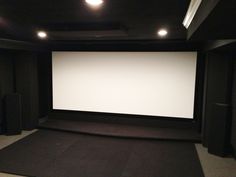 an empty theater room with black carpet and white screen on the wall in front of it