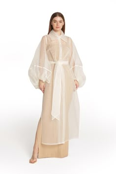 Editor's Notes: This dress has a touch of romance to it with its long jacket and dramatic sleeves. The winter white fabric adds elegance. The slip dress underneath is a bronze-beige color to add a subtle contrast and the length is a few inches longer than the jacket. The jacket is made from soft organza fabric with a hint of shimmer. It features dramatic balloon sleeves, piping details, wide collar and self tie belt. It has an inner dress in soft viscose satin. Style it with gold colored jewelry Organza Overcoat Dress, Luxury Outerwear With Sheer Long Sleeves, Organza Abaya, Organza Overcoat, Luxury Sheer Fall Outerwear, Elegant Luxury Sheer Outerwear, Dramatic Sleeves Dress, Dress With Outer, Outer Organza