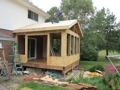 a man standing on top of a wooden roof next to a house under construction in the yard