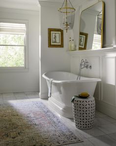 a white bath tub sitting in a bathroom next to a rug and framed pictures on the wall