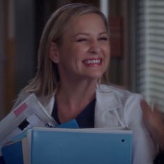 a woman in a white lab coat holding files and folders smiling at the camera