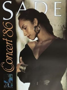 a woman in black dress standing next to a wall with the words sade on it