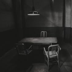 an empty room with a table and two chairs in front of a lamp hanging from the ceiling