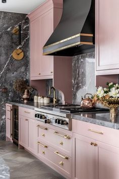 a kitchen with pink cabinets and marble counter tops, gold pulls on the oven hood