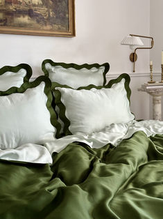 a bed with green sheets and pillows in a room next to a painting on the wall