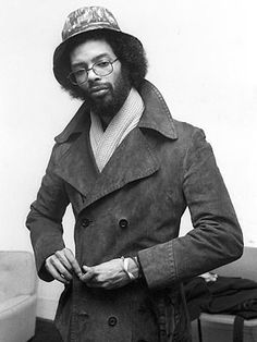 a black and white photo of a man in a trench coat with a hat on