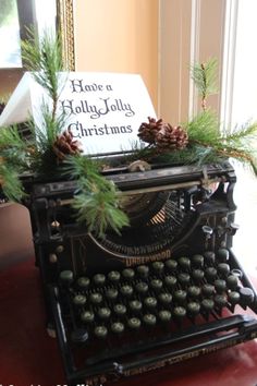 an old fashioned typewriter decorated with pine cones and greenery sits in front of a sign that says have a holly jolly christmas