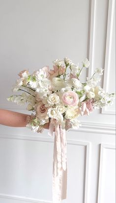 a bridal bouquet with pink and white flowers on the bride's arm in front of a door