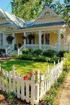 a white picket fence in front of a house with flowers growing on the lawn and bushes around it