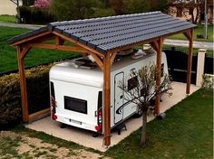 an rv parked under a wooden structure in the grass next to a tree and bushes