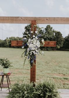 a cross decorated with flowers and greenery in front of a wooden bench on the grass