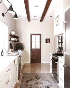 a kitchen with white cabinets and wooden beams on the ceiling, along with an area rug