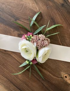 a bouquet of flowers is tied to a white ribbon on a wooden table with leaves