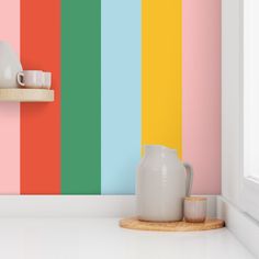 a white vase sitting on top of a counter in front of a rainbow striped wall