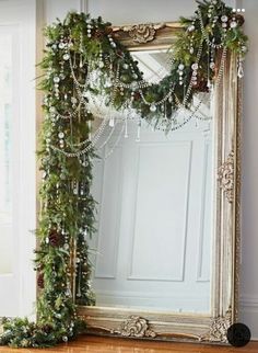 a large mirror sitting on top of a wooden floor next to a christmas wreath and garland