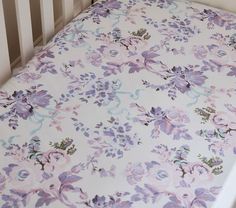 a baby crib with a pink and blue flowered sheet on the bottom half