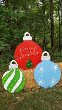 three christmas ornaments sitting on top of hay bales in front of trees and bushes