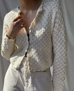 a woman wearing a white crochet jacket and pants with her hands on her chest