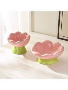 two pink and green dishes sitting on top of a white table next to a mirror