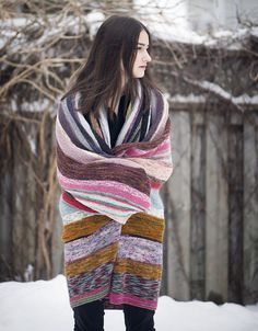 a woman standing in the snow wearing a multicolored shawl and black boots