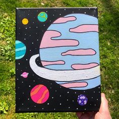 a hand holding up a small canvas with planets painted on it