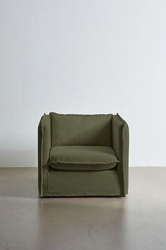 a green chair sitting on top of a floor next to a white wall with a plant in it