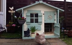 a chicken is standing in front of a small house with flowers and potted plants