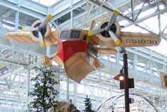 a model airplane hanging from the ceiling in a building with trees and other decorations around it