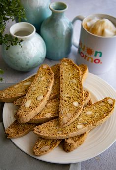 a white plate topped with slices of bread next to a cup and vase filled with flowers