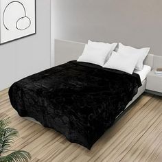 a large black blanket on top of a bed in a bedroom next to a plant