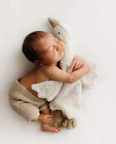 a baby sleeping with a stuffed animal in his arms on a white background that looks like he is holding it