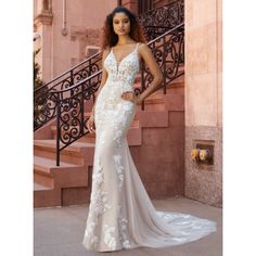 a woman standing in front of some stairs wearing a wedding dress with flowers on it