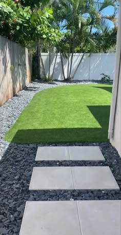 a small yard with grass and stepping stones in the ground, next to a white fence