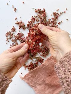 two hands are holding some red stuff in front of them on a white surface with other pieces of fabric