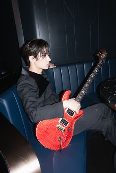 a man sitting in a blue chair holding a red guitar and looking at the camera