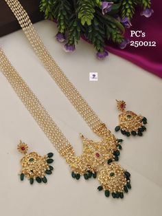 two necklaces with green stones and gold chains on a white table next to purple flowers