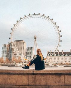 a woman sitting on the edge of a wall next to a ferris wheel