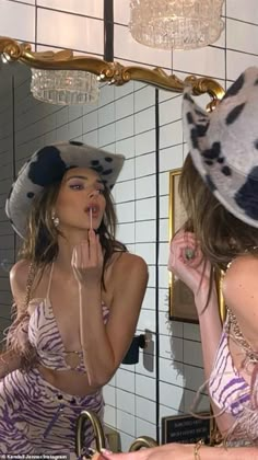 a woman is brushing her teeth in front of a mirror wearing a hat and dress