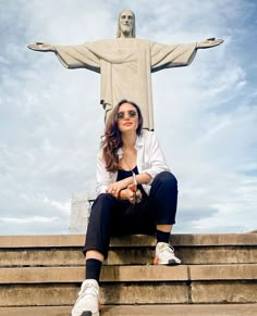 a woman sitting on steps in front of the statue of jesus with her arms crossed