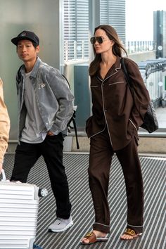 a man and woman walking through an airport with luggage on their feet, one carrying a suitcase