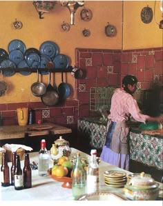 a woman in a kitchen preparing food on a counter top with lots of plates and pans hanging from the wall