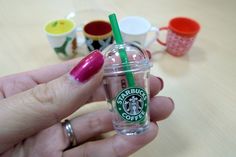 a person holding a starbucks cup with a green straw in it's mouth and pink nail polish