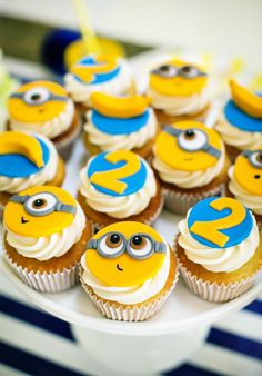 cupcakes with yellow and blue frosting are arranged on a white cake plate