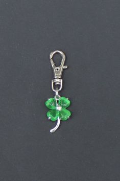 a green clover charm on a black surface with a metal hook in the shape of a four leaf clover