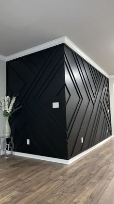 an empty room with wood flooring and black wallpaper on the walls, along with a vase filled with flowers